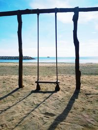 Swing hanging at beach against sky