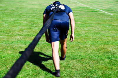 Full length rear view of man tied with rope walking on field