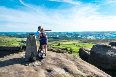 Full length of couple standing on rock formation while looking at landscape against sky