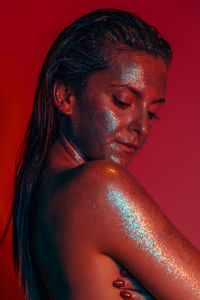 Close-up of shirtless young woman with glitters in darkroom