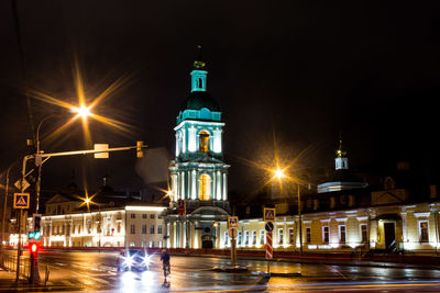 Illuminated street light by building against sky at night