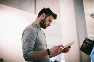 Side view of young man reading document at home