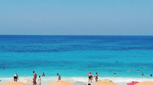 People on beach against clear blue sky