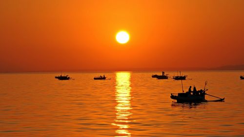 Silhouette boat sailing on sea against orange sky