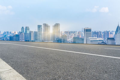 Road by buildings against sky in city