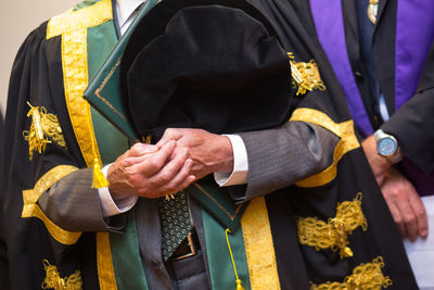 Midsection of man with certificate wearing gown during graduation ceremony