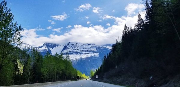 Road amidst trees and snowcapped mountains against sky