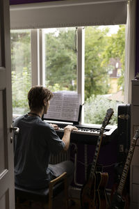 Rear view of man reading music note while practicing piano at home