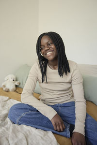 Smiling female teenager with braided hair sitting on bed at home