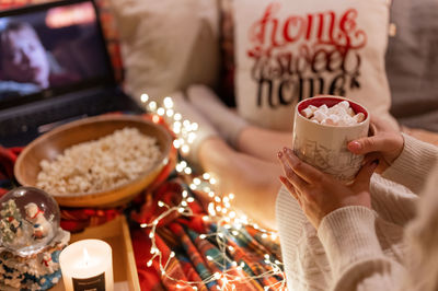 Cup of cocoa or coffee drink with marshmallows in female holding hands of woman in knitted sweater