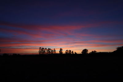 Silhouette trees on field against sky during sunset