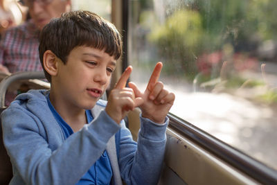 Boy sitting by window while gesturing in tram