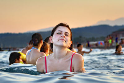 Portrait of young woman swimming in sea against clear orange sky