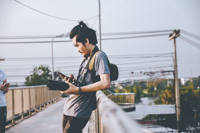 Young man using mobile phone while walking on bridge