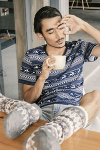 Full length of lazy young man holding coffee cup while sitting at home