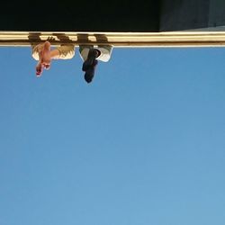 Low angle view of people sitting on wall against clear sky