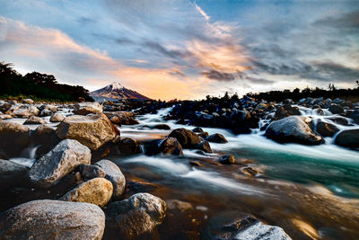 Rocks in sea against sky during sunset