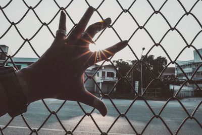 Hand holding chainlink fence against sky