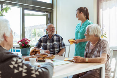 Smiling senior man and nurse talking while having breakfast at nursing home