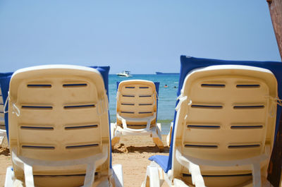 Close-up of deck chairs on beach against blue sky