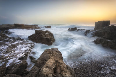 Rocks in sea against sky during sunset