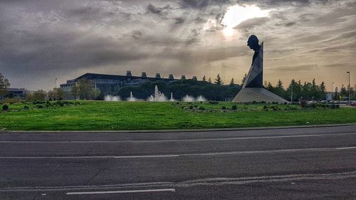 Road by building against cloudy sky