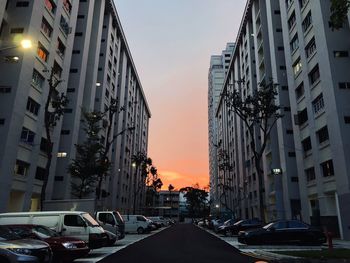 Traffic on road amidst buildings in city against sky at sunset