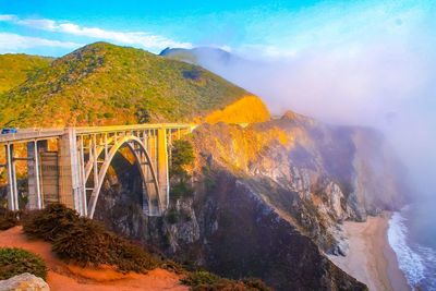 Arch bridge over mountain against cloudy sky