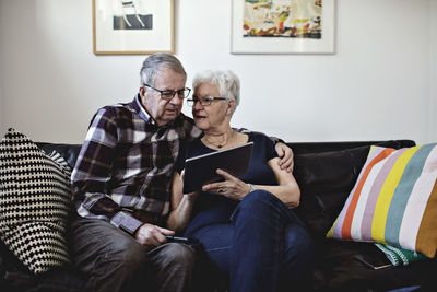 Senior couple sitting on sofa while sharing digital tablet against wall at home