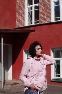 Young woman with closed eyes standing against red building