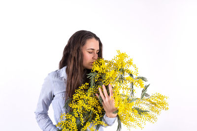 Young woman holding yellow flower against white background