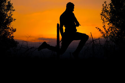 Silhouette man by orange tree against sky during sunset