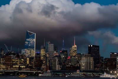 Illuminated skyscrapers in city against cloudy sky