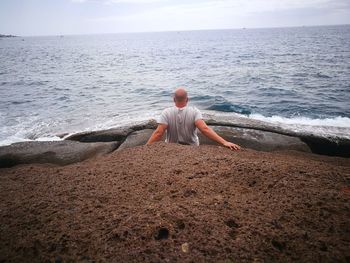 Rear view of man looking at sea while sitting on rock