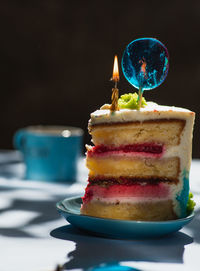 Plate with slice of tasty homemade raspberry cake. colorful lollipop swirl on stick. burning candle