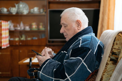 Side view of senior man using mobile phone at home