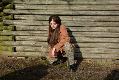 Young girl crouches on the floor in front of old wooden planks, looks down