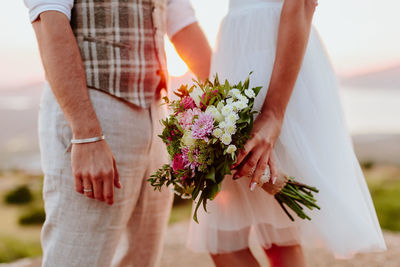 Midsection of bride and groom standing against sky