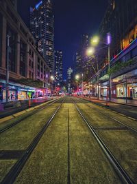 Illuminated railroad tracks amidst buildings in city at night