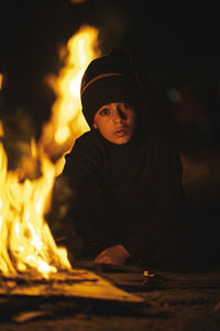 Portrait of boy sitting by bonfire at night