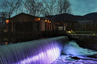 Water flowing over illuminated buildings against sky at night