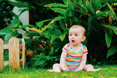 Cute baby girl with mouth open sitting on land against plants