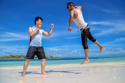 Full length of friends enjoying on beach against sky