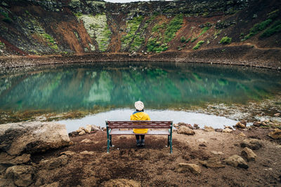 Rear view of woman sitting on bench by lake