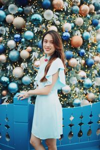 Portrait of smiling young woman standing by christmas tree outdoors