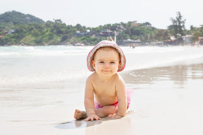 Smiling little girl is playing with sand near to sea on a background of tropical beach.