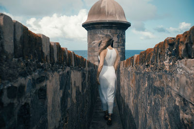 Rear view of woman standing on wall against sky