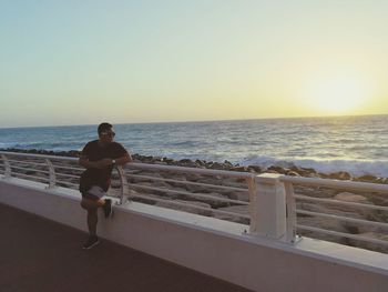 Man standing by swimming pool against sea against clear sky