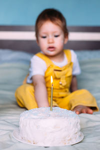 Llittle cute toddler is celebrating her birthday at home on bed with cake