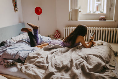 Young woman using mobile phone while lying on bed at home